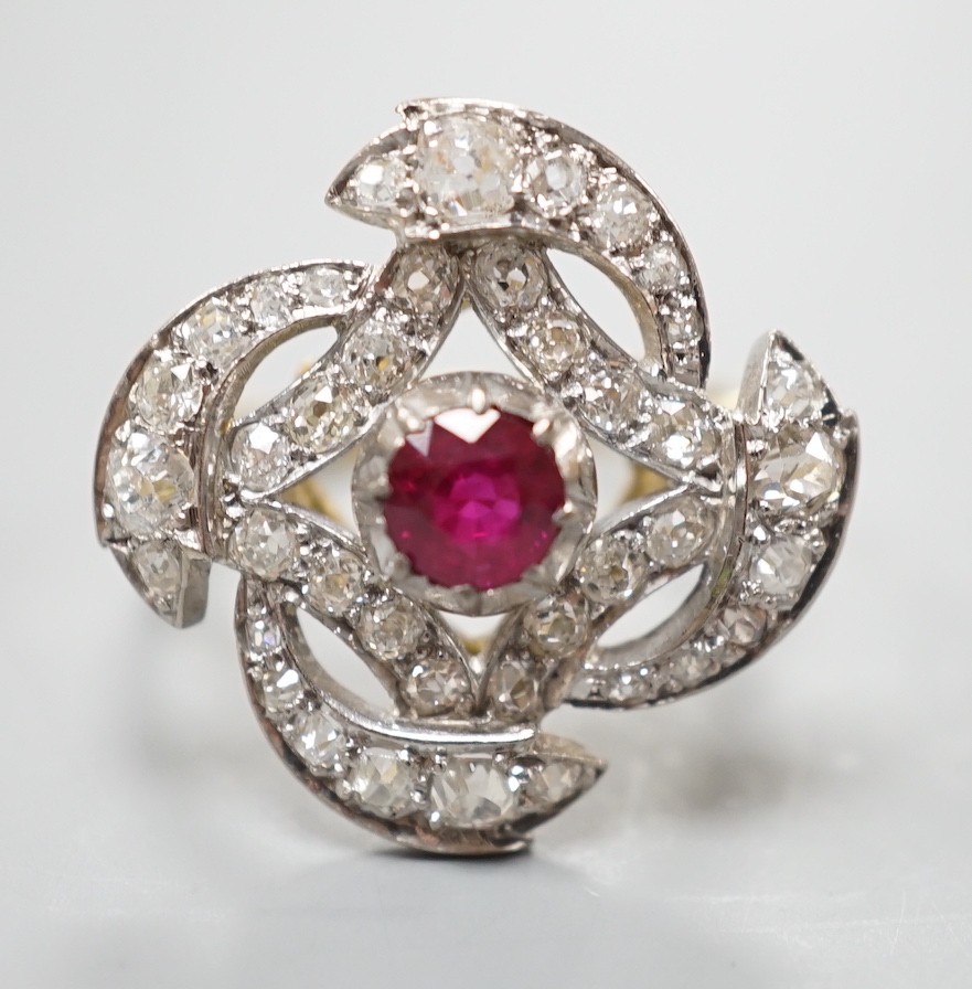 A yellow metal, ruby and diamond cluster set dress ring, in a pierced scroll setting, size O, gross weight 6 grams.